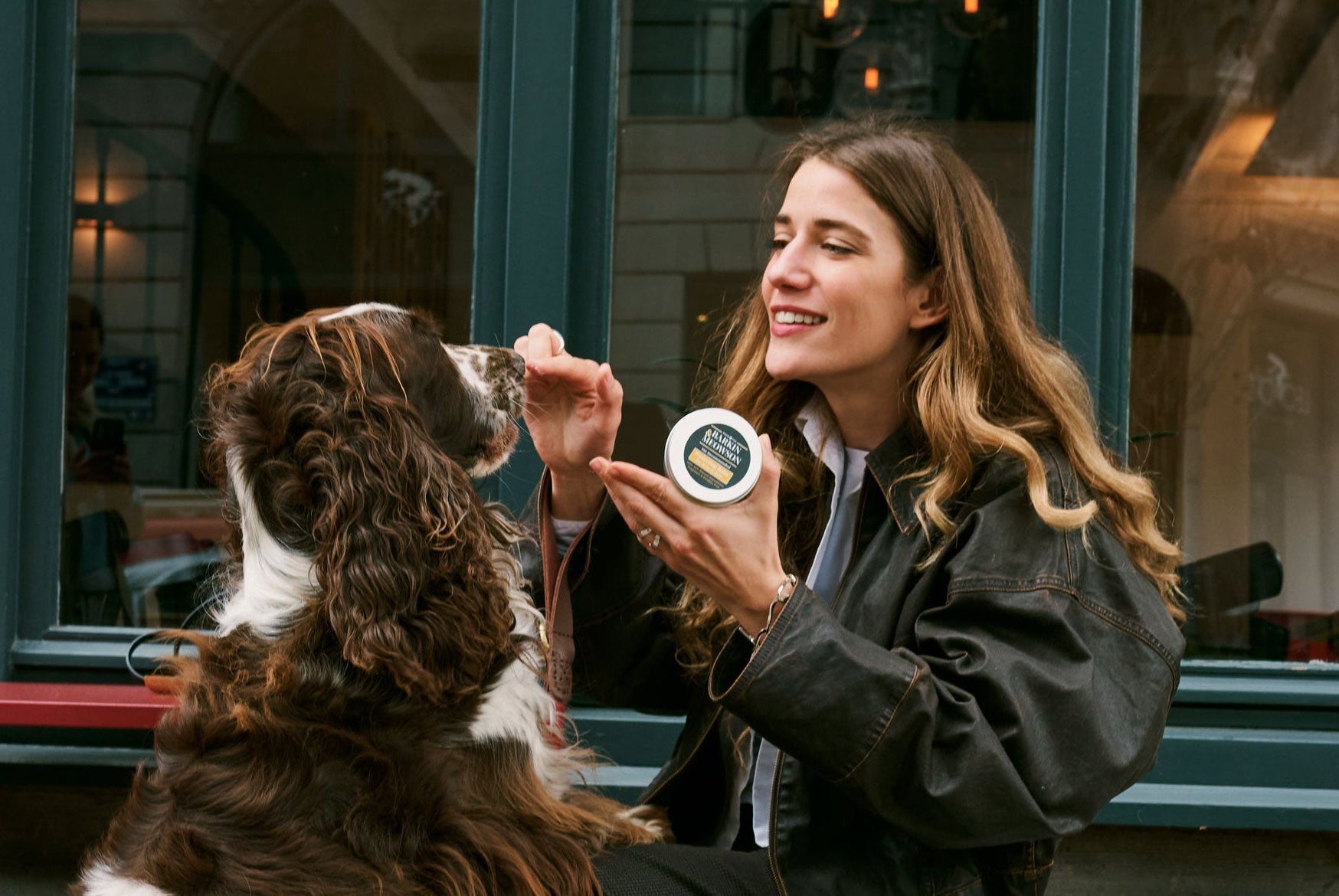Woman sitting with a dog at an outdoor cafe, holding a coffee cup.