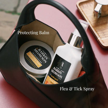 Barking Meowson pet care products including a jar and bottle in a black bag on a pink surface.
